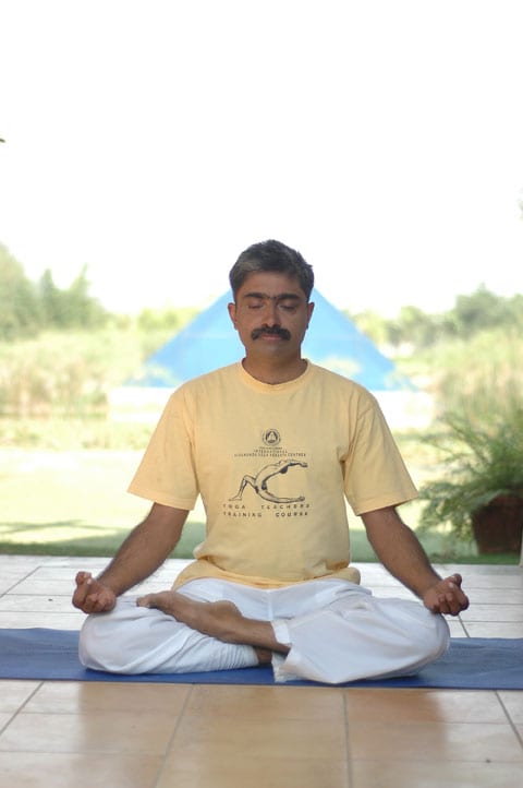 meditation - a man sitting cross-legged with eyes closed on a mat outdoors.