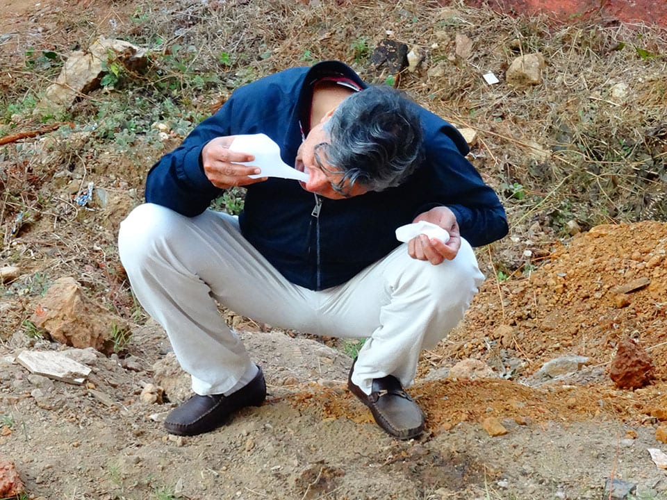 jal neti kriya - a man rinsing one nostril from a neti pot, crouched outdoors.