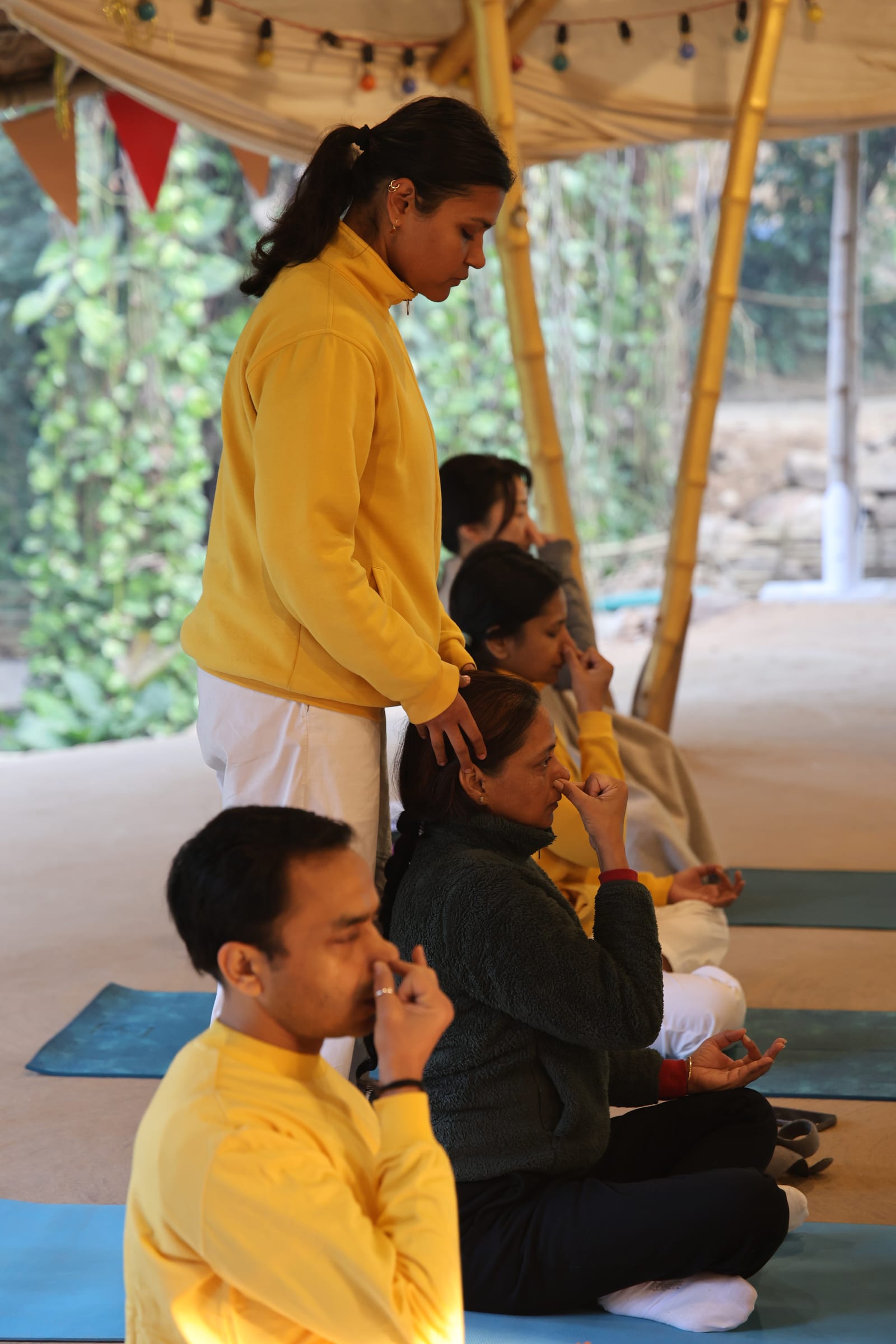 A teacher resting a hand on a seated student as the group practices Anuloma Viloma (alternate nostril breathing)